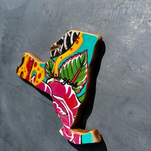 May include: Wooden New York state-shaped magnet with a colorful floral design. The magnet features a vibrant mix of colors, including pink, teal, yellow, and green, with the words "New York" in cursive. The edges are a natural wood color.