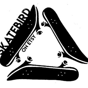 May include: Black and white graphic of three skateboards arranged in a triangle. The word "SKATEBIRD" is printed on one skateboard, with "ON ETSY" below it. The skateboards have wheels and are set against a white background.