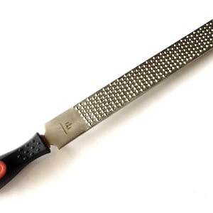 May include: A metal rasp with a textured surface for woodworking. It has a black and red handle for grip. The rasp is designed for shaping and smoothing wood surfaces. The tool is used in carpentry and other woodworking projects.