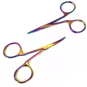 Puede incluir: Dos tijeras iridiscentes de color arcoíris con bucles para los dedos. Las tijeras tienen una punta afilada y un mecanismo de bloqueo. Están diseñadas para cortar con precisión, posiblemente para manualidades o uso médico.