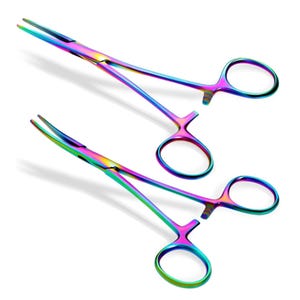 Puede incluir: Dos pinzas quirúrgicas de color arcoíris, también conocidas como hemostáticas, se muestran sobre un fondo blanco. Las pinzas están hechas de acero inoxidable y tienen un acabado liso y pulido.