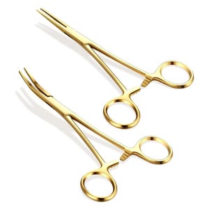 May include: Two gold-colored surgical clamps with curved tips and locking mechanisms. The clamps are used for holding tissue during surgery.