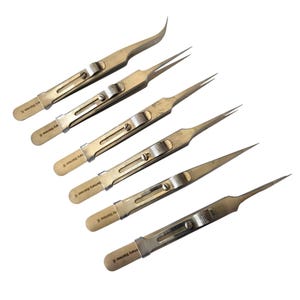 May include: A set of six silver-toned metal tweezers arranged diagonally. Each tool features a sliding locking mechanism with a textured grip and a tapered tip. The handle of each tweezer is stamped with the text Germany Stainless.
