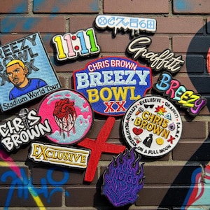 May include: A selection of embroidered patches with diverse designs and text, such as "Breezy Bowl," "Chris Brown," and "Exclusive." The patches display bright colours and are arranged on a brick wall with graffiti art.