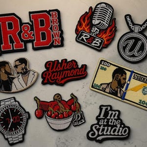 May include: A collection of embroidered patches with various designs. Includes patches with the text "R&B", a microphone, a dollar bill with a portrait, a watch, and the text "I'm at the Studio".