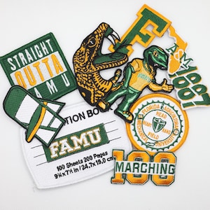 Puede incluir: Un conjunto de parches bordados en verde, dorado y blanco. Los parches presentan textos como "STRAIGHT OUTTA AMU" y "FAMU", junto con una mascota de serpiente y "MARCHING 100". Un parche es un cuaderno de 24,7 x 19,0 cm.