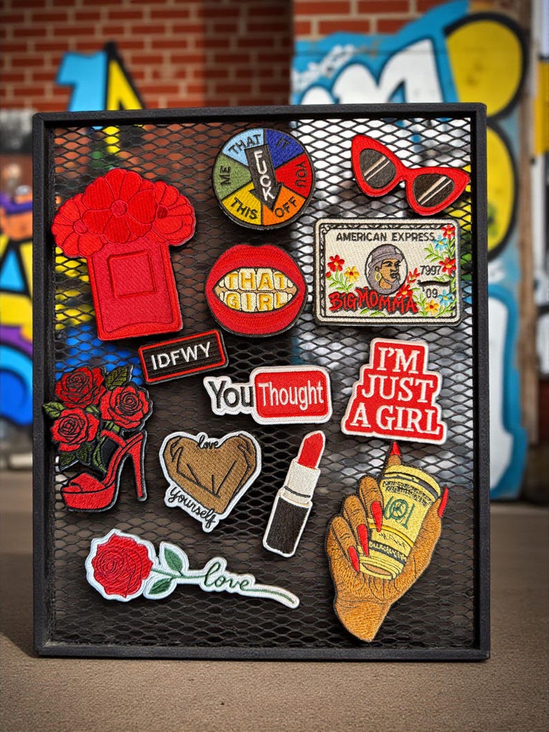 May include: A collection of embroidered patches on a black mesh background. Patches include a red high-heeled shoe, a lipstick, a coffee cup, and text patches that say "I'M JUST A GIRL" and "YOU THOUGHT".