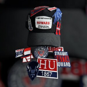 May include: Black baseball cap with multiple embroidered patches. Patches include text that reads "HOWARD", "1867", and "STRAIGHT OUTTA HOWARD". The cap also features a buffalo logo and a patch that reads "COMPOSITION BOOK HOWARD".