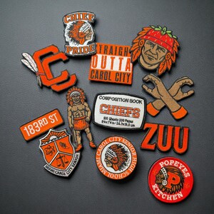 Op de afbeelding: Een verzameling geborduurde patches in oranje, wit en rood. De patches tonen teksten als "Chief Pride", "Carol City" en "Popeyes Kitchen", samen met verschillende illustraties, waaronder een Indiaanse chef en gekruiste handen.