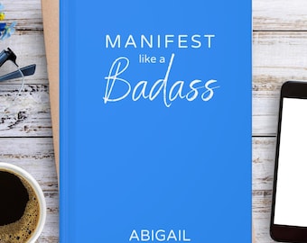 May include: A bright blue hardcover journal featuring the white text "MANIFEST like a Badass" in a combination of sans-serif and script fonts, with the name "ABIGAIL" printed in white sans-serif capital letters at the bottom of the front cover.