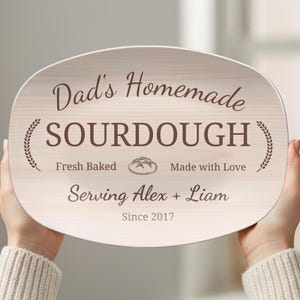 May include: Oval wooden serving board with the text "Dad's Homemade SOURDOUGH" in a decorative font. The board includes the phrases "Fresh Baked," "Made with Love," and "Serving Alex + Liam Since 2017." Wheat sprigs and a bread illustration are also featured.