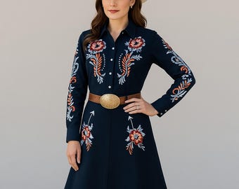 May include: A navy blue dress with long sleeves and floral embroidery in red, orange, and white. The dress features a button-down front, a brown belt with a gold buckle, a white cowboy hat, and brown cowboy boots.