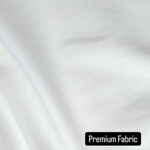 May include: Close-up of white fabric with subtle diagonal texture. The fabric is draped, creating soft folds and shadows. The text "Premium Fabric" is displayed in a black rectangle at the bottom of the image. The fabric appears to be smooth and high-quality.