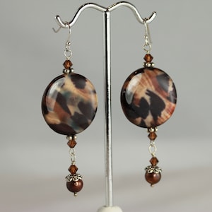 May include: A pair of long dangle earrings with brown and black patterned round beads, brown crystal beads, and silver accents.
