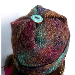 May include: A quick folded hat made from colourful, textured yarn with a teal button on top. The hat is folded in a way that creates a unique and stylish look.