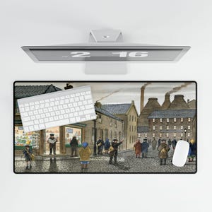 May include: A rectangular mouse pad featuring a detailed illustration of a street scene with buildings, people, and a cobblestone road. A white keyboard and mouse are on the pad. The monitor above shows the numbers "2 16".