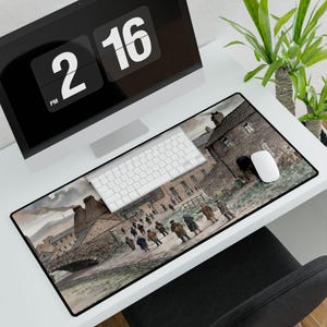May include: Rectangular mouse pad featuring a historical watercolor painting of a town scene with people walking on a road. The pad is black-edged and sits on a white desk with a computer, keyboard, and mouse.