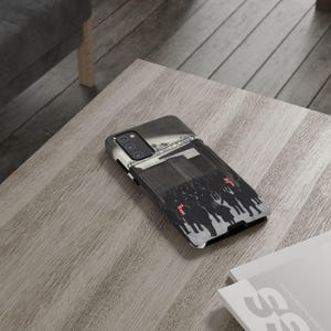 May include: A black and white phone case with a graphic of people on horseback. The case is rectangular and made of a hard material. The design includes red accents. The case is suitable for a mobile phone.