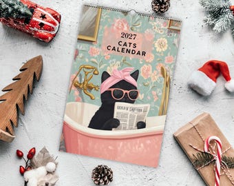 May include: A 2027 wall calendar featuring an illustration of a black cat wearing a pink headband and pink sunglasses while sitting in a pink bathtub and reading a newspaper. The background shows a floral wallpaper and gold fixtures.