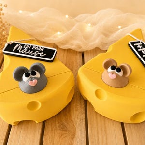 Könnte beinhalten: Zwei gelbe Käse-förmige Boxen, jeweils mit einer 3D-Mausfigur. Eine Maus ist grau mit rosa Nase, die andere ist braun. Jede Box hat ein schwarzes Etikett mit weißem Text.