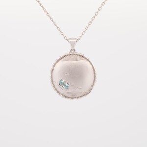 May include: A silver necklace with a round pendant featuring a light blue gemstone. The pendant has a textured, circular design.