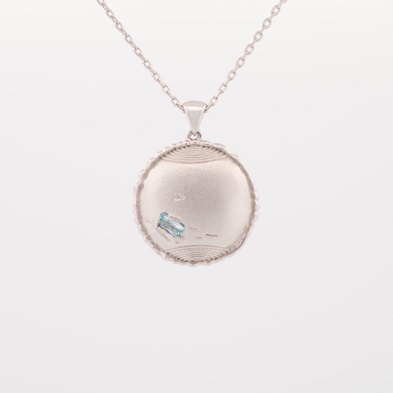 May include: A silver necklace with a round pendant featuring a light blue gemstone. The pendant has a textured, circular design.