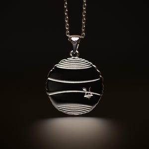 May include: Silver pendant necklace with a round, textured disc featuring a stylized design. The back of the pendant has a small inscription.