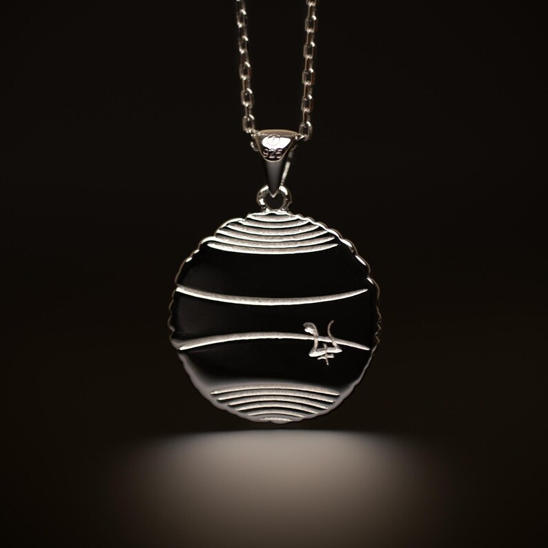 May include: Silver pendant necklace with a round, textured disc featuring a stylized design. The back of the pendant has a small inscription.