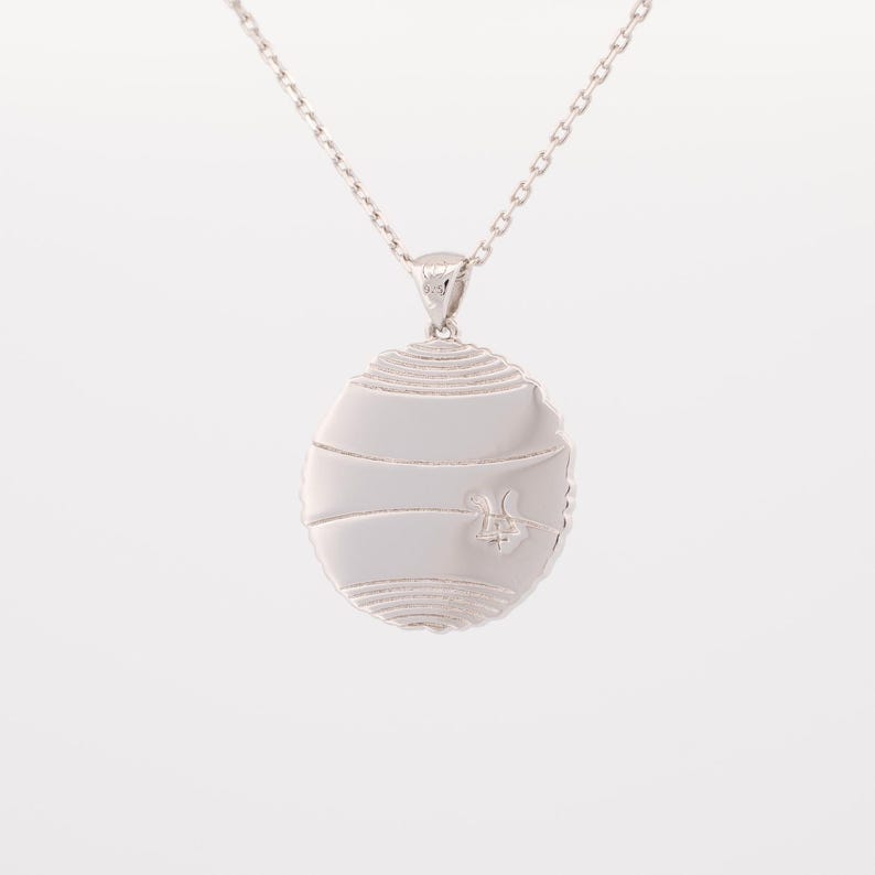 May include: Silver pendant necklace with a circular design featuring a textured surface and a small bee design in the center.