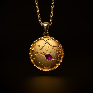 May include: A gold necklace with a round pendant featuring a textured surface with a small purple gemstone in the center.
