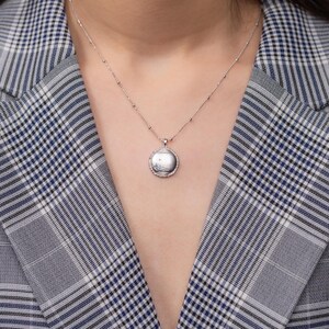 May include: A silver necklace with a round pendant featuring a delicate design. The pendant is on a silver chain with small beads.