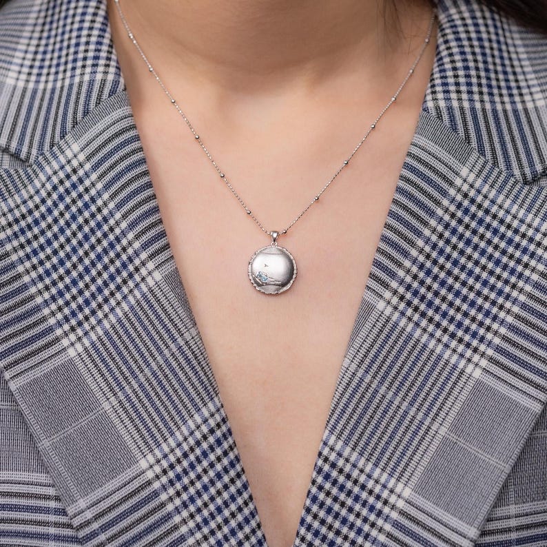 May include: A silver necklace with a round pendant featuring a delicate design. The pendant is on a silver chain with small beads.