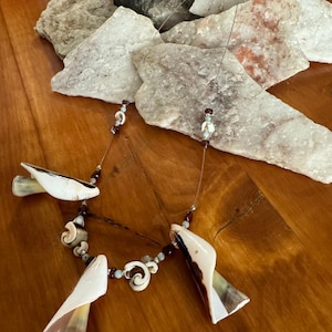 以下が含まれることがあります： 天然の貝殻と小さな濃い赤色のビーズで作られたネックレス。ネックレスには、渦巻き模様の大きなユニークな貝殻が3つ付いています。