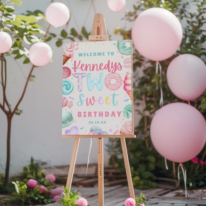 Puede incluir: Un caballete de madera exhibe un letrero colorido que dice "Welcome to Kennedys Two Sweet Birthday". El letrero est&aacute; decorado con ilustraciones de dulces y colores pastel. Globos rosas y arreglos florales rodean el caballete.