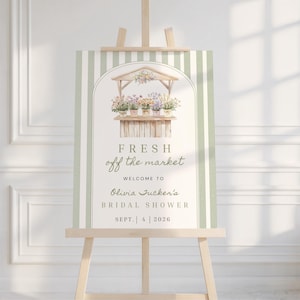 Puede incluir: Un letrero rectangular sobre un caballete de madera con un borde de rayas verde salvia y blanco. El centro muestra una ilustración en acuarela de un puesto de flores con plantas en macetas, seguido del texto FRESH off the market WELCOME TO Olivia Tucker's BRIDAL SHOWER SEPT. 4 2026.