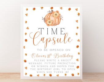 May include: A white framed sign with the words "Time Capsule" in elegant script, adorned with a pumpkin and fall leaves. The sign reads "To be opened on Olivias 18th Birthday". It encourages guests to write messages.