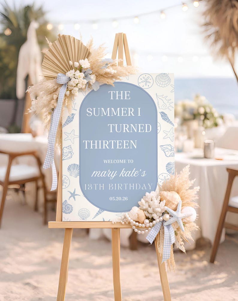 以下が含まれることがあります： 木製のイーゼルには、「The Summer I Turned Thirteen」というテキストが青いアーチ型のフレームで表示された看板が飾られています。看板は貝殻とヒトデで装飾され、ドライフラワーとリボンで飾られています。