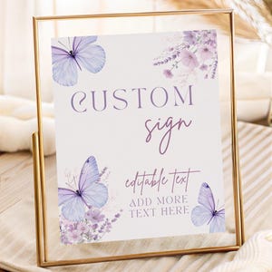 May include: A rectangular sign in a thin gold metal frame featuring light purple butterfly illustrations and floral accents. The text reads CUSTOM sign, editable Text, and ADD MORE TEXT HERE in a mix of serif and script fonts on a white background.