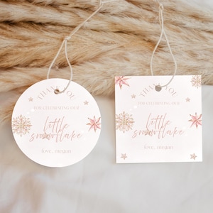 May include: Two white gift tags with string, one round and one square. Both tags have the text "THANK YOU FOR CELEBRATING OUR little snowflake love, megan" in pink and gold, with snowflake and star designs.