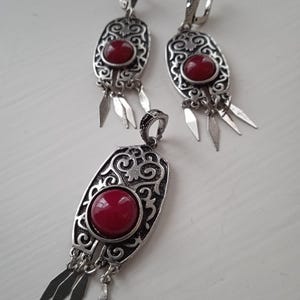 Peut inclure: Un ensemble de collier et boucles d'oreilles en argent avec des accents de pierres précieuses rouges. Le pendentif et les boucles d'oreilles présentent des motifs floraux complexes et des accents pendants.