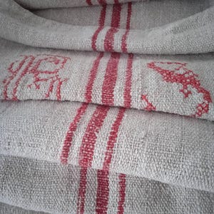 Op de afbeelding: Een stapel linnen stof met rode strepen. De stof is gevouwen en heeft een ruwe textuur.