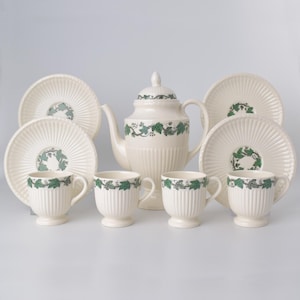 May include: Cream-colored tea set with a teapot, cups, and saucers. The set features a ribbed design and is decorated with green leaf patterns. The teapot has a lid, and the cups have handles. The saucers and cups have a green leaf design in the center.