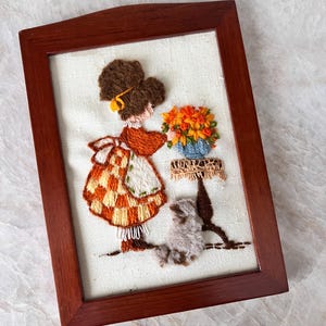 Arte bordado vintage hecho a mano: Niña con flores y gato peludo. Tapiz textil 3D con marco de madera.