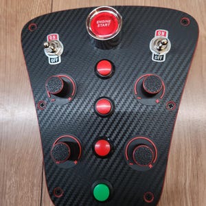 May include: A black carbon fibre control panel with red trim. It has an "ENGINE START" button, toggle switches marked "ON" and "OFF", red buttons, knobs, and a green button. The panel is secured with screws.