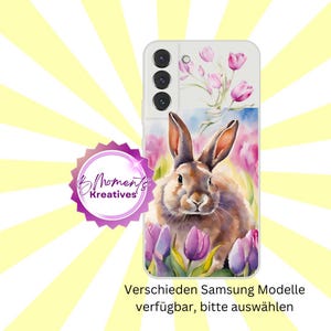 Puede incluir: Una funda de teléfono blanca con un diseño de acuarela de un conejo marrón rodeado de tulipes moradas. La funda del teléfono tiene una protuberancia de cámara con tres lentes.