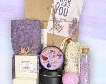 May include: A gift box with a lavender theme, including a purple towel, soap, a candle with dried flowers, a bath bomb, and a bottle of bath salts. A card with the text "I wish life brings you happiness and joy" is tied to the box.