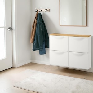 Könnte beinhalten: Eine moderne Eingangsszene mit einem weißen Schuhschrank mit heller Holzplatte und vier Klapptüren. Über dem Schrank hängt ein Spiegel mit Holzrahmen. Ein beiger Teppich und eine Garderobe aus Holz mit Jacken vervollständigen den Raum.