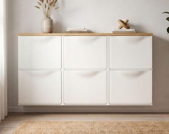 Peut inclure: Un meuble de rangement mural blanc à six compartiments rectangulaires avec un plateau en bois clair. Sur le dessus, on trouve un vase beige avec des herbes séchées, une pile de livres et une petite sculpture géométrique en bois.