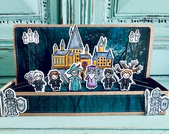 May include: A pop-up card featuring a castle, characters, and candles. The card has a teal background with a brown border. The castle is yellow and gray, and the characters are dressed in robes. Two knights are on the front of the card.