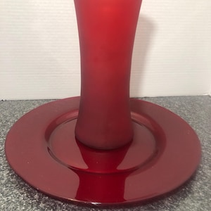 May include: A red glass vase with a frosted finish sits on a red glossy charger plate.